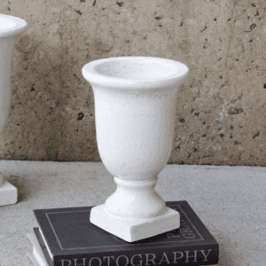 White decorative urn on a black photography book against a concrete wall.